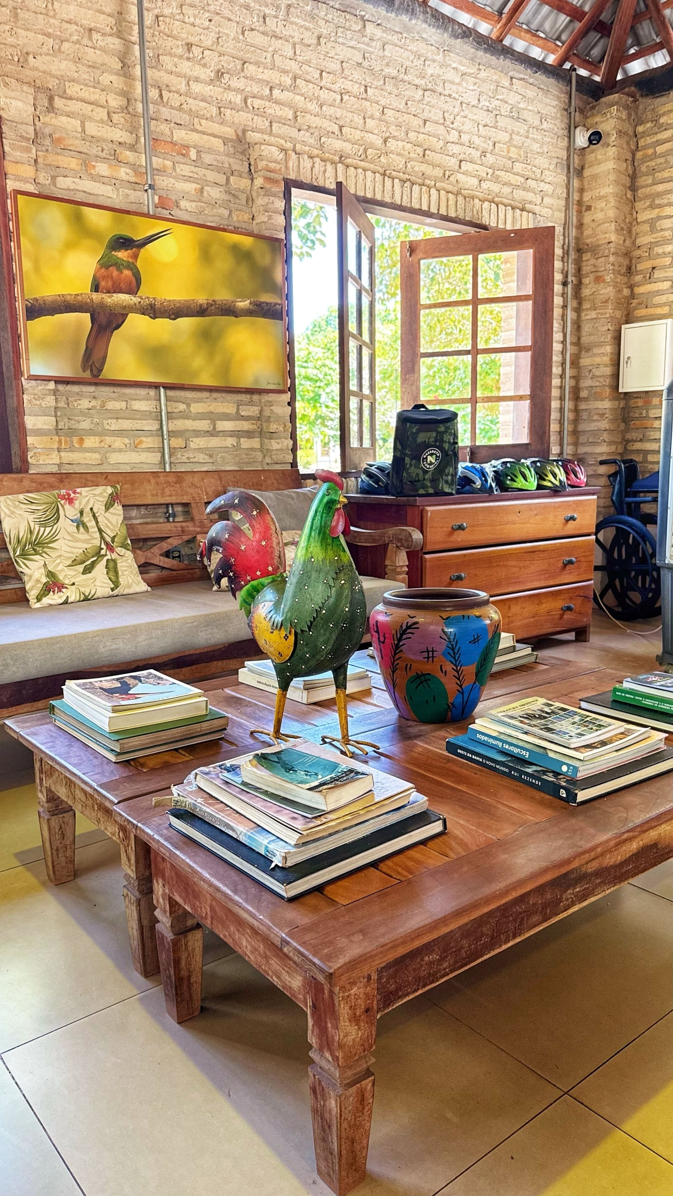 Una habitación rústica con una mesa de centro de madera, una escultura de gallo colorido y una estantería llena de libros.