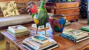 A rustic room with a wooden coffee table, a colorful rooster sculpture, and a bookshelf with books.