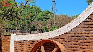 Uma grande roda de madeira, uma parede de tijolos e um moinho de vento ao fundo.