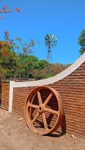 A large wooden wheel, a brick wall, and a windmill in the background. - Nazareth Eco Hotel (José de Freitas)
