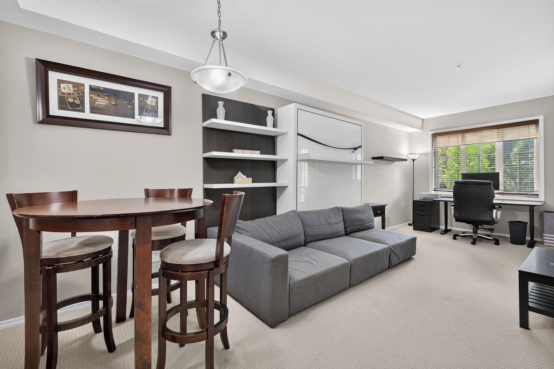 A modern living room with a dining table, gray sofa, and a black office chair.