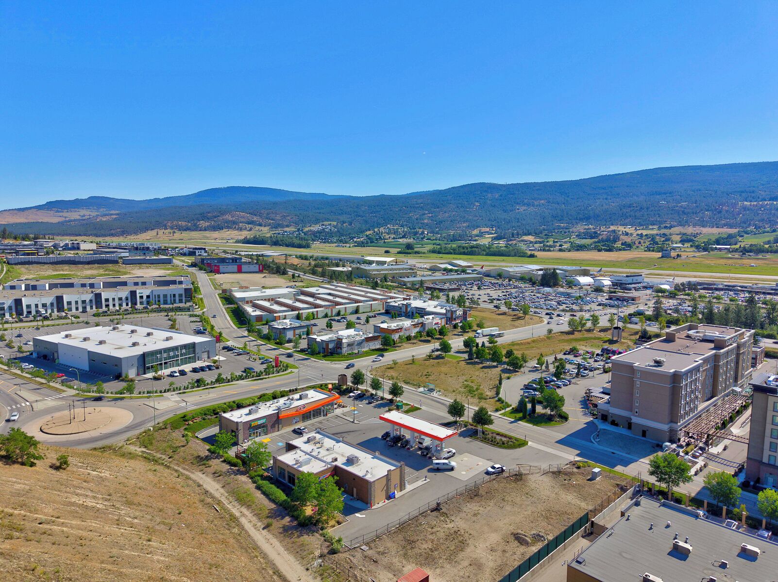 An industrial area with large buildings, parking lots, and a gas station.