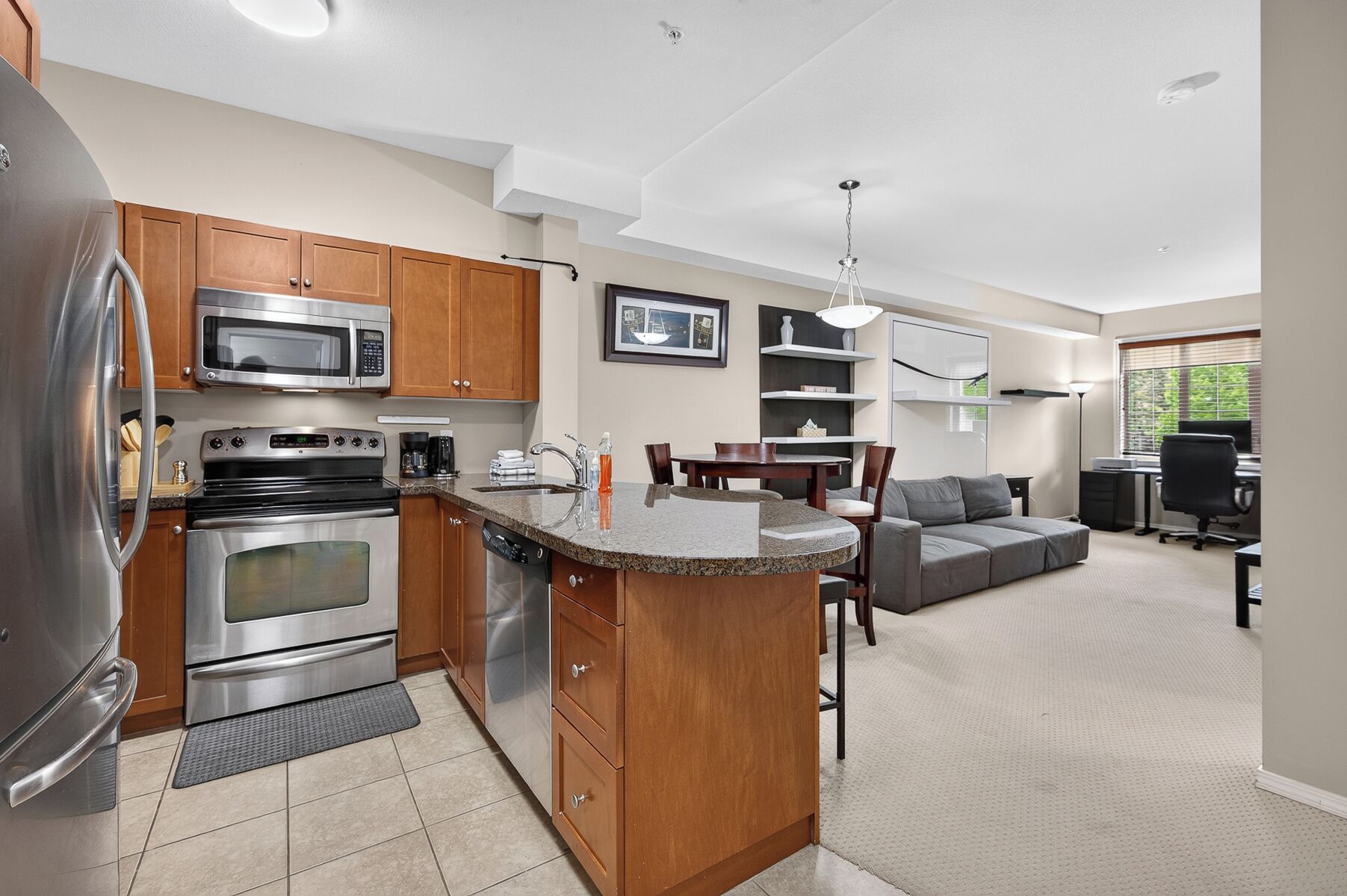 A modern kitchen with built-in appliances, a dining area with a sofa, and a workspace with a desk and chair.
