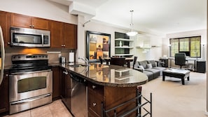 A modern kitchen with stainless steel appliances, a dining area with a sofa and table, and a workspace with a computer. - Mountain View w Pool and Hot Tub 2213 (Kelowna)