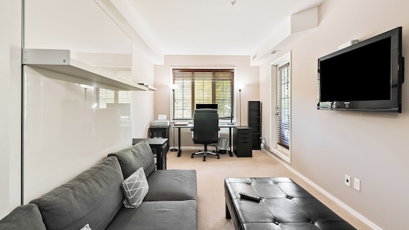 A modern living room with a sofa, a coffee table, a TV, and a desk with a computer. - Mountain View w Pool and Hot Tub 2213 (Kelowna)