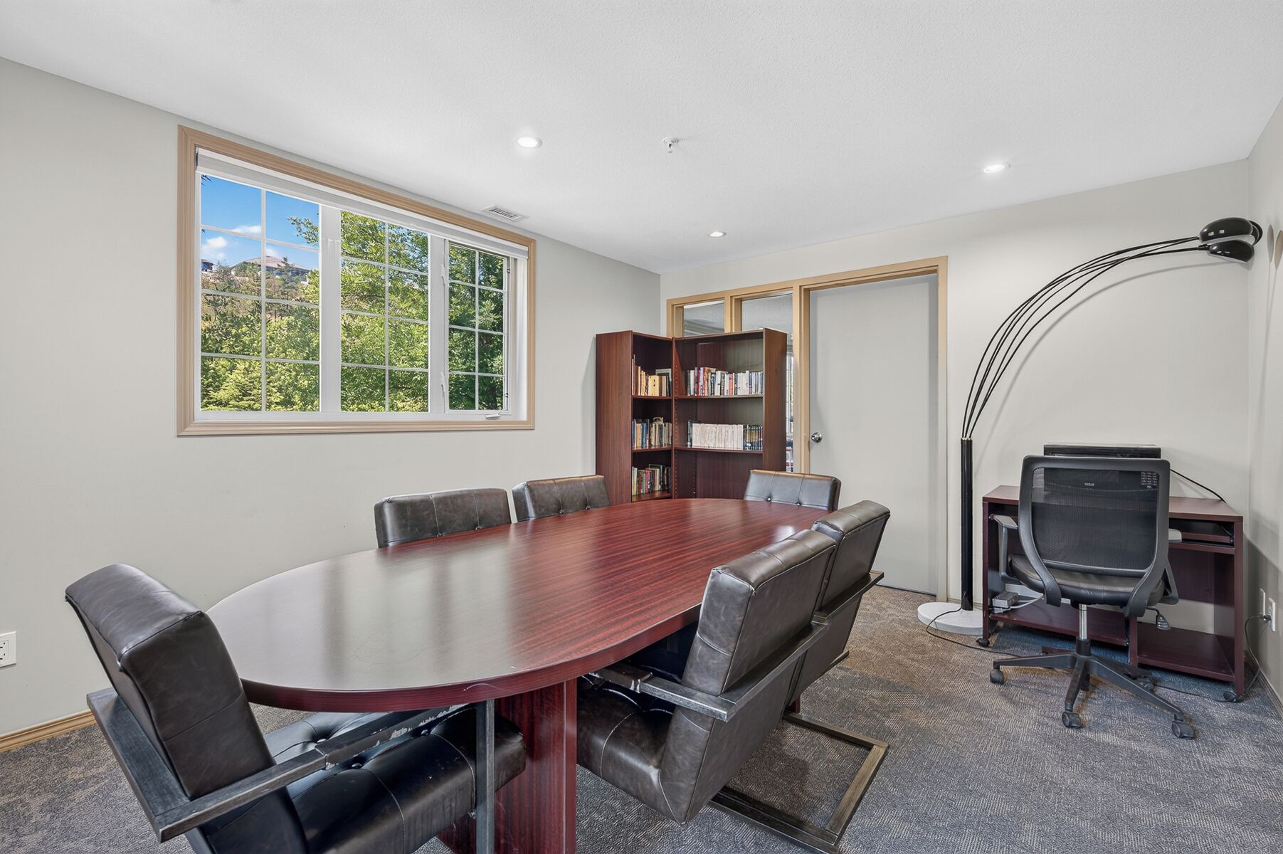 Une salle de conférence dotée d’une grande table ovale, de fauteuils en cuir, d’une bibliothèque et d’un bureau avec un ordinateur.