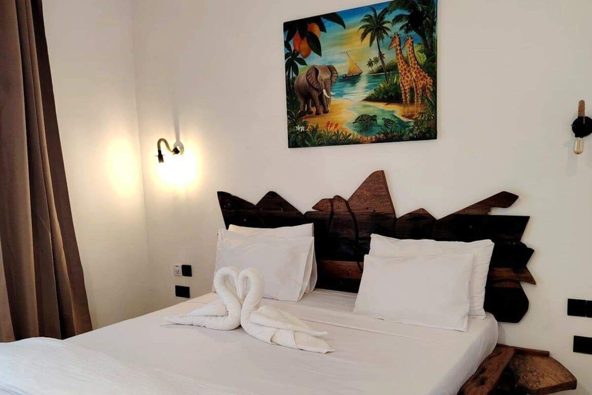 Un llit amb estructura de fusta, roba de llit blanca i un quadre amb una escena tropical a la part superior.