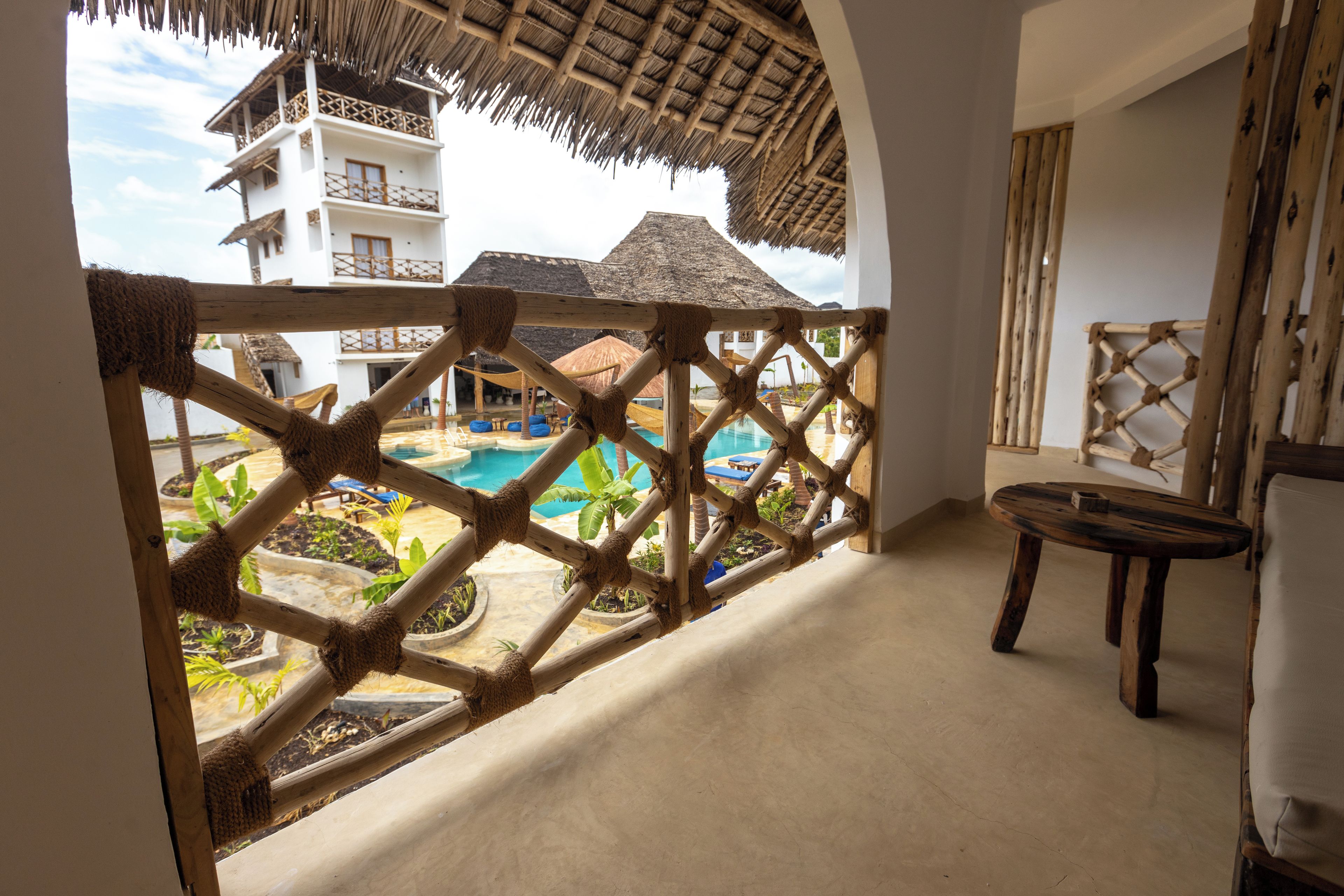 A room with a view of a pool and a thatched-roof building.