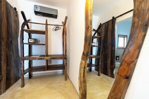 A wooden shelf unit with a small safe, a wall-mounted air conditioning unit, and a mirror reflecting part of the room. - Faro Resort (Nungwi)