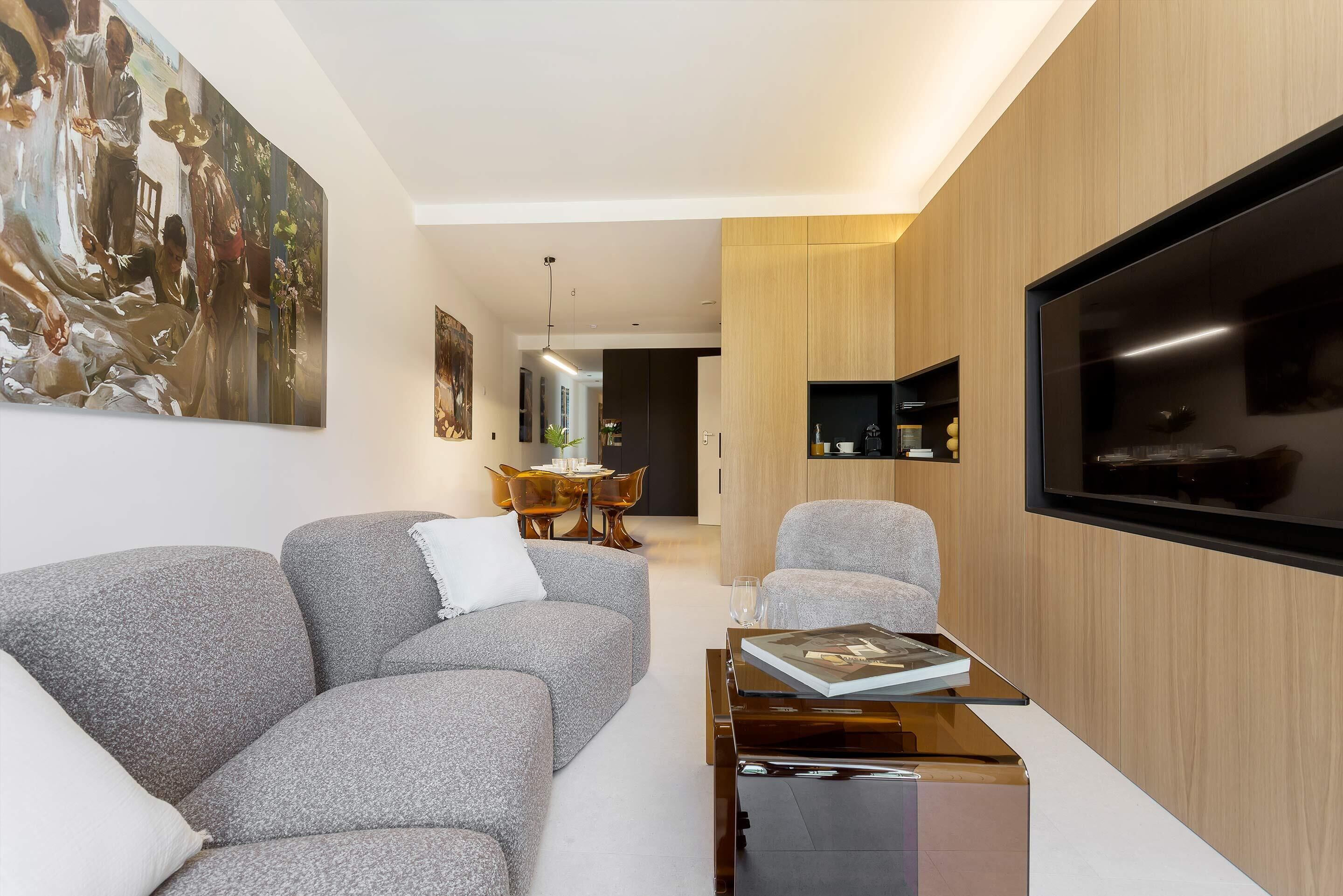 A modern living room with a grey sofa, a coffee table, a flat-screen TV, and a large painting on the wall.