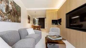 A modern living room with a grey sofa, a coffee table, a flat-screen TV, and a large painting on the wall.