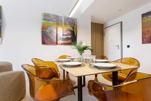 Een eetruimte met een houten tafel, oranje stoelen en een schilderij aan de muur.