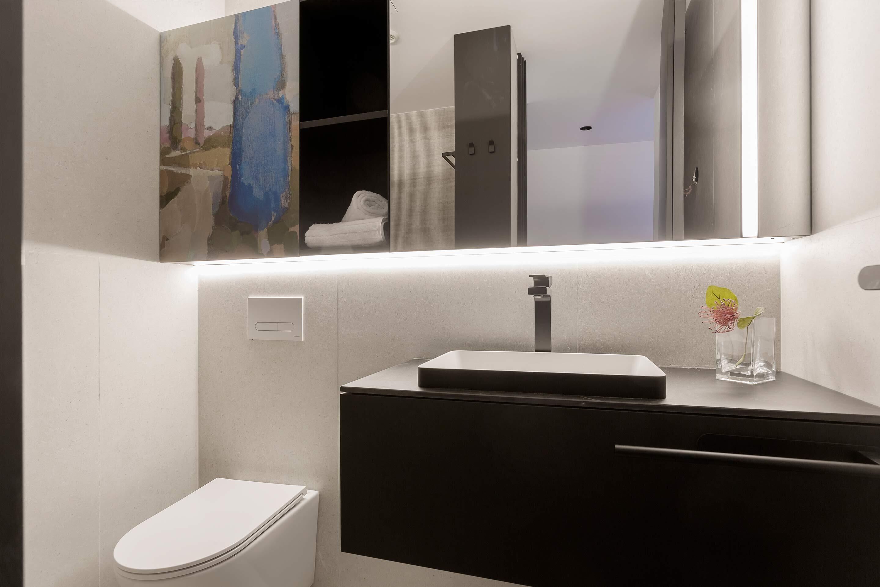 Een moderne badkamer met toilet, wastafel en spiegel erboven, en een handdoekrek.