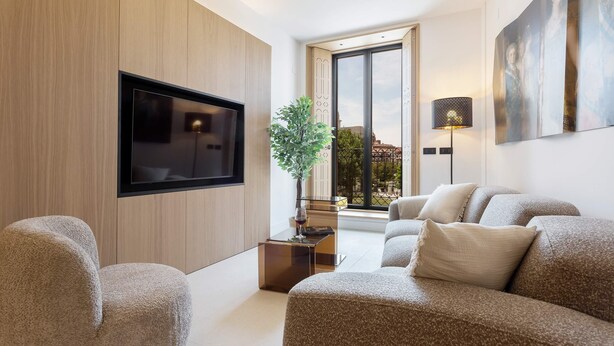 Una sala de estar moderna con un televisor de pantalla plana, una mesa de centro, un conjunto de sofás, una planta en maceta y un amplio ventanal con vistas.