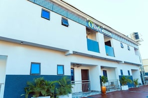 Un edificio moderno con un letrero que dice 'Olive Apartments'. Presenta una fachada plana con un diseño geométrico en la parte superior, numerosas ventanas y una entrada portonada.