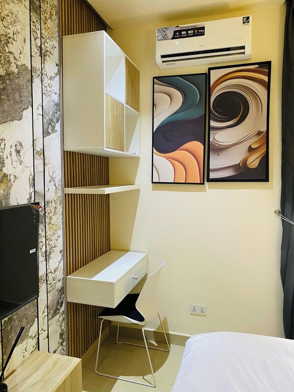 Una habitación de hotel moderna con un escritorio blanco, una silla, una cama y dos cuadros abstractos en la pared.