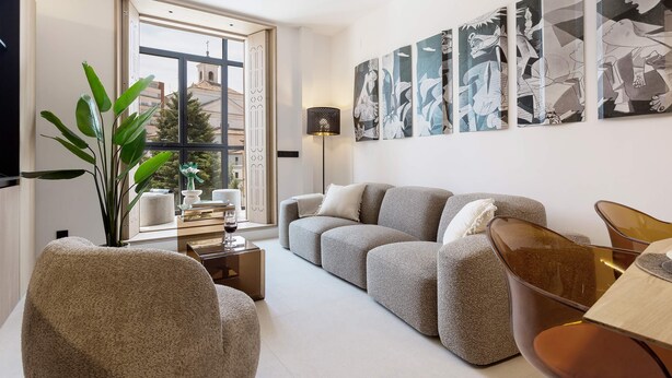 A modern living room with a grey sofa, a coffee table, a plant, and abstract art on the wall.