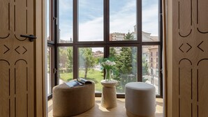 A room with large windows, a wooden door with geometric cutouts, and two ottomans.