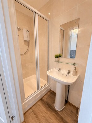 Ein Badezimmer mit Duschkabine, Waschbecken auf Säule und Spiegel über dem Waschbecken.