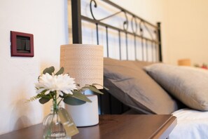 Un letto con testiera, un comodino con una lampada e un vaso con fiori.