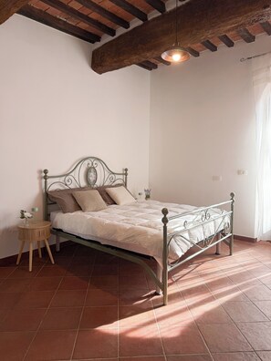 Una cama individual con estructura metálica, una mesita de noche con lámpara y una lámpara colgante.