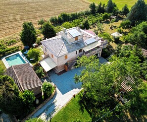 A large house with a swimming pool, surrounded by lush greenery and fields.