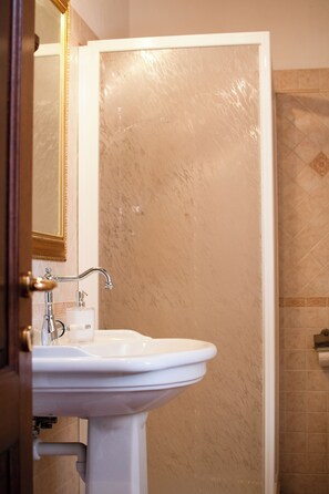 Un baño con lavamanos blanco, un espejo y una puerta que da a una zona de ducha.