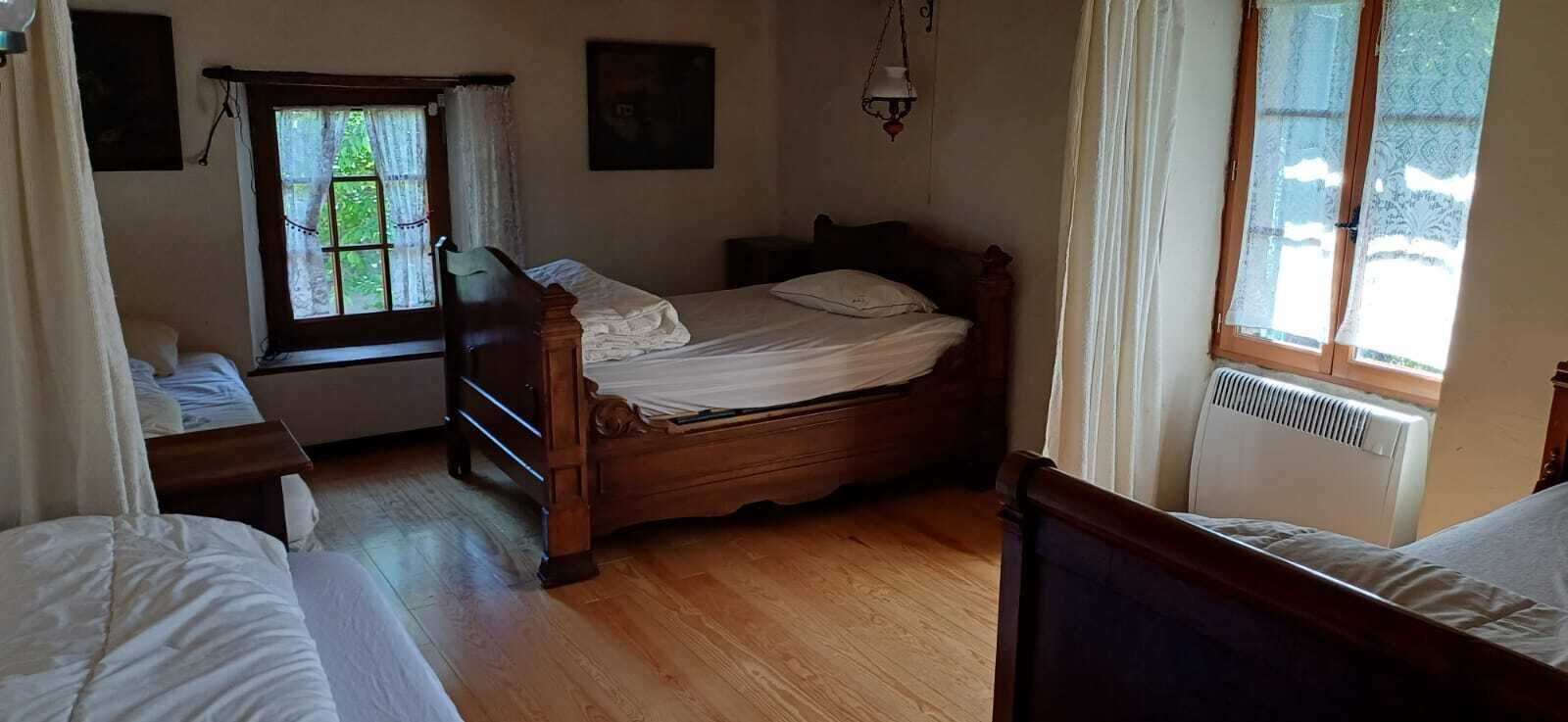 Une chambre avec un lit en bois, une fenêtre avec des rideaux, un radiateur et une lampe suspendue.