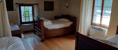 Une chambre avec un lit en bois, une fenêtre avec des rideaux, un radiateur et une lampe suspendue.