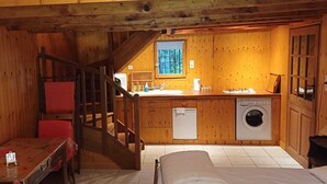A cabin with a wooden interior, a dining area with a table and chairs, a kitchen with a sink and washing machine, and a staircase. - The Berger-By Farm and its two outbuildings, in the heart of the Two Lakes region (Pressins)