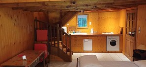 A cabin with a wooden interior, a dining area with a table and chairs, a kitchen with a sink and washing machine, and a staircase. - The Berger-By Farm and its two outbuildings, in the heart of the Two Lakes region (Pressins)