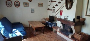 En stue med blå sofa, træbord, fjernsyn, pejs og diverse ting på væggene.