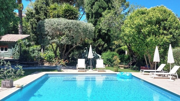A rectangular swimming pool with lounge chairs and umbrellas, surrounded by lush greenery and a small building with a red roof. - Charming holiday cottage with pool-pétanque-table tennis-foosball-BBQ-parking (Roujan)