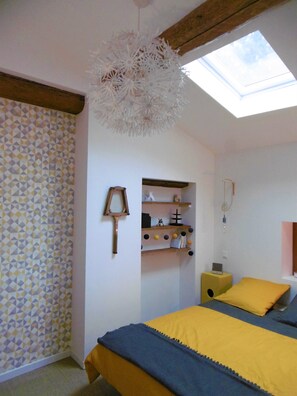 Ein Schlafzimmer mit Oberlicht, einem Bett mit gelb-blauer Bettwäsche, einer Wand mit Muster und einem Regal mit verschiedenen Gegenständen.