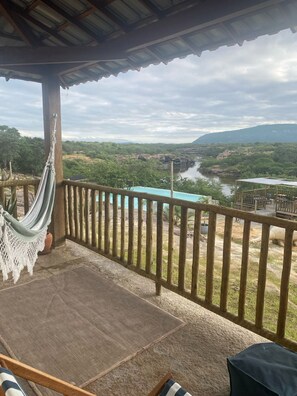Un balcó amb cadira d'hamaca, vista d'un riu i una serralada de muntanyes a la distància.