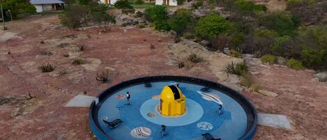 Un espacio exterior circular con una estructura amarilla en el centro y un suelo azul decorado con motivos planetarios.