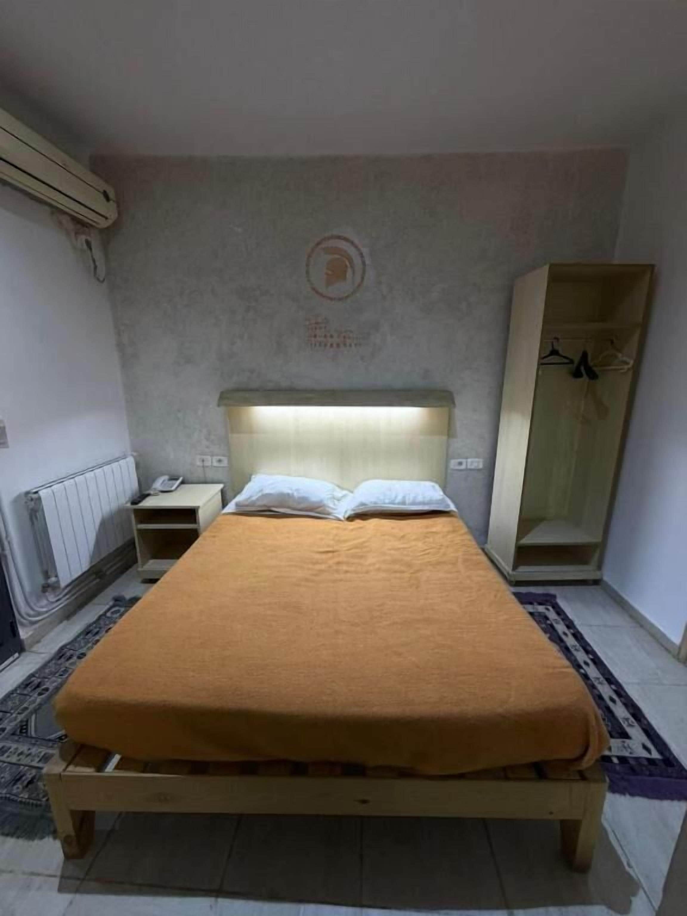 Una cama individual con cabecera, una mesita de noche, un armario y un radiador.