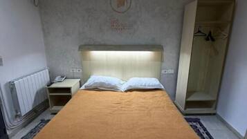 Una cama individual con cabecera, una mesita de noche, un armario y un radiador.