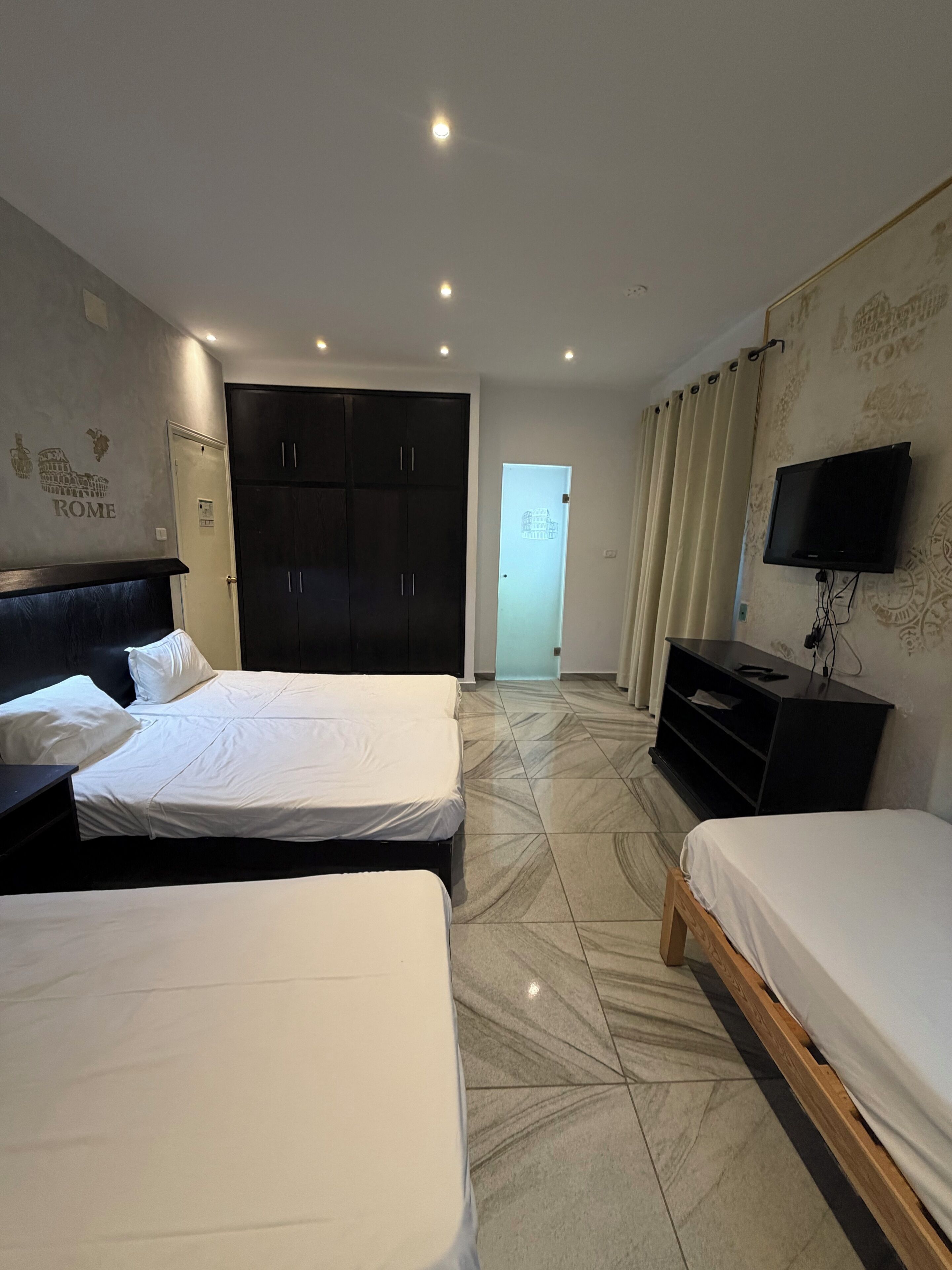 Habitación de hotel con dos camas, un armario, televisión y puerta que da a un baño.