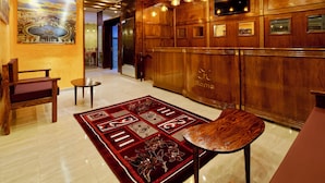 A lobby with a wooden reception desk, a red patterned rug, and a painting of a cityscape.
