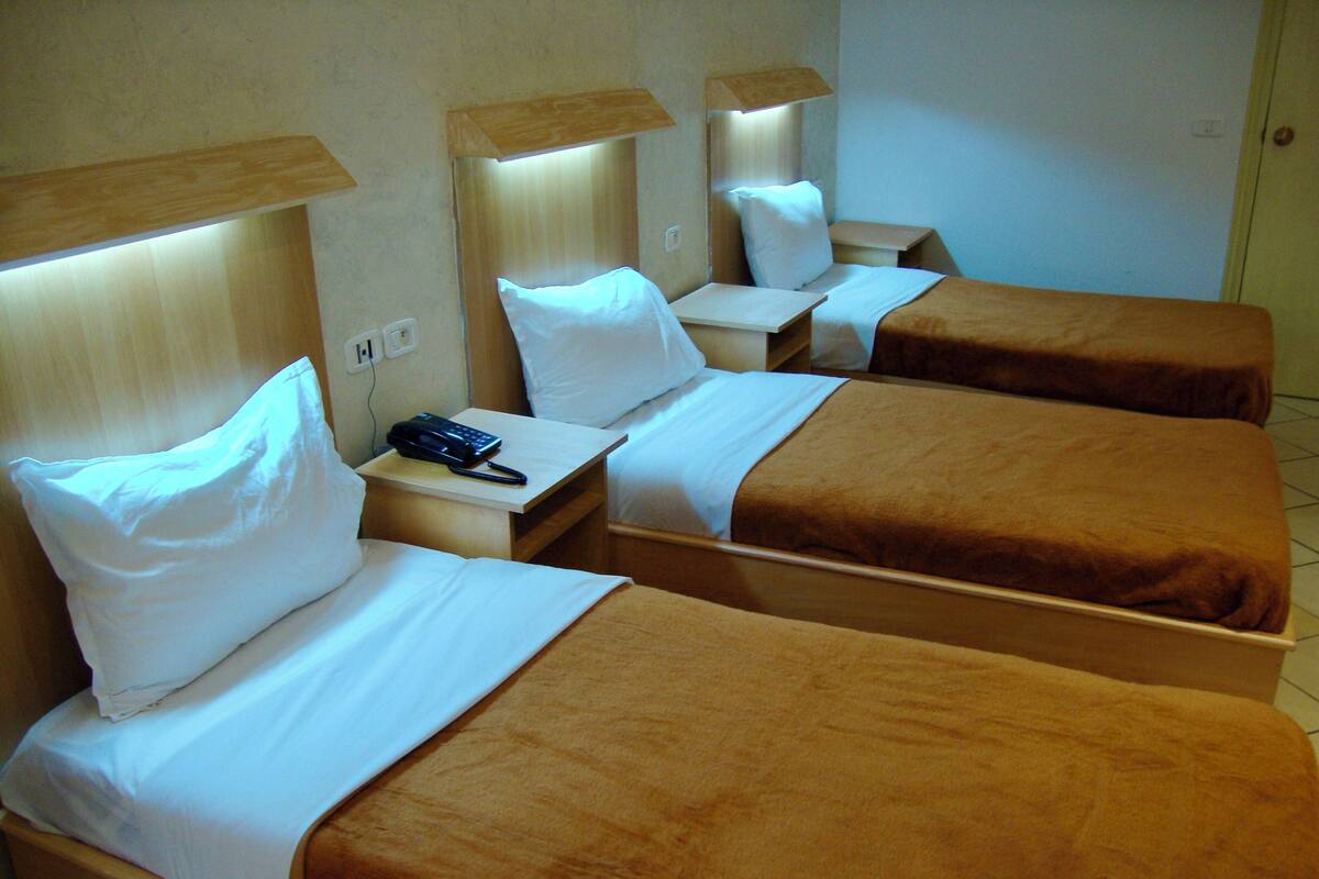 Une chambre d’hôtel avec trois lits simples, chacun doté d’une tête de lit en bois et d’une table de chevet.
