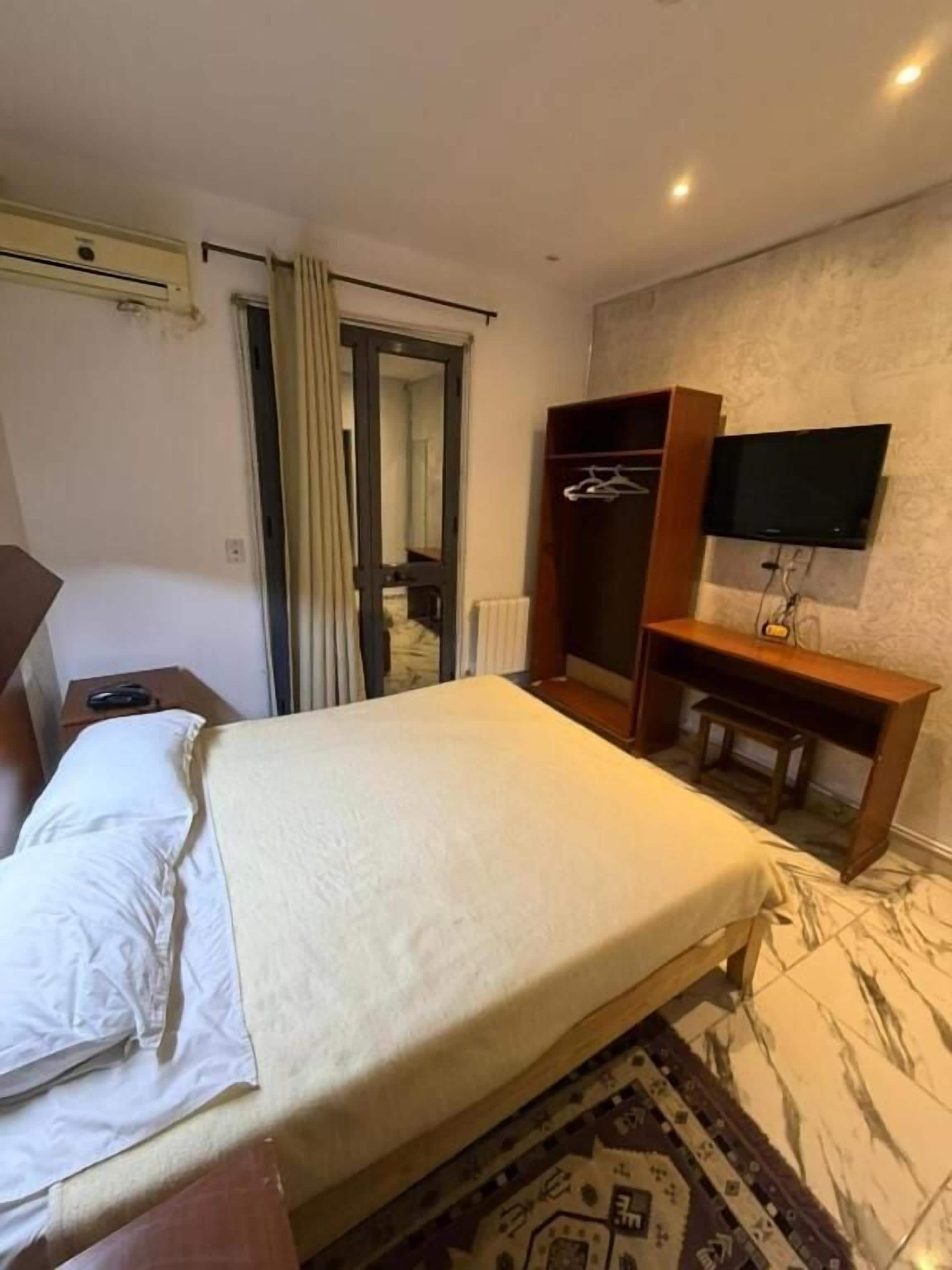 Una habitación de hotel con una cama, un escritorio, un televisor y un armario.