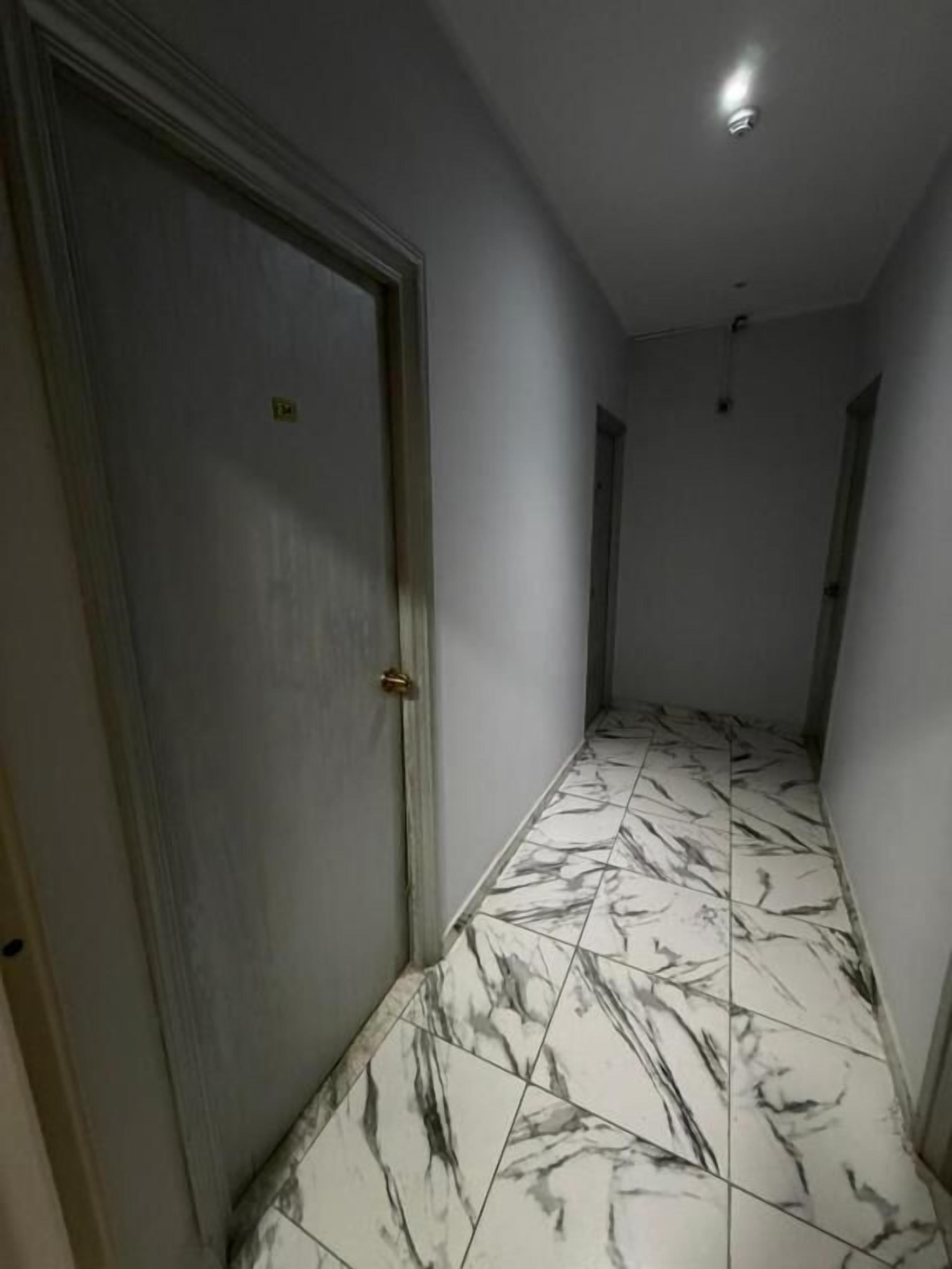 A hallway with marble flooring and a door on the left.