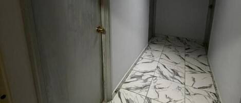 A hallway with marble flooring and a door on the left.