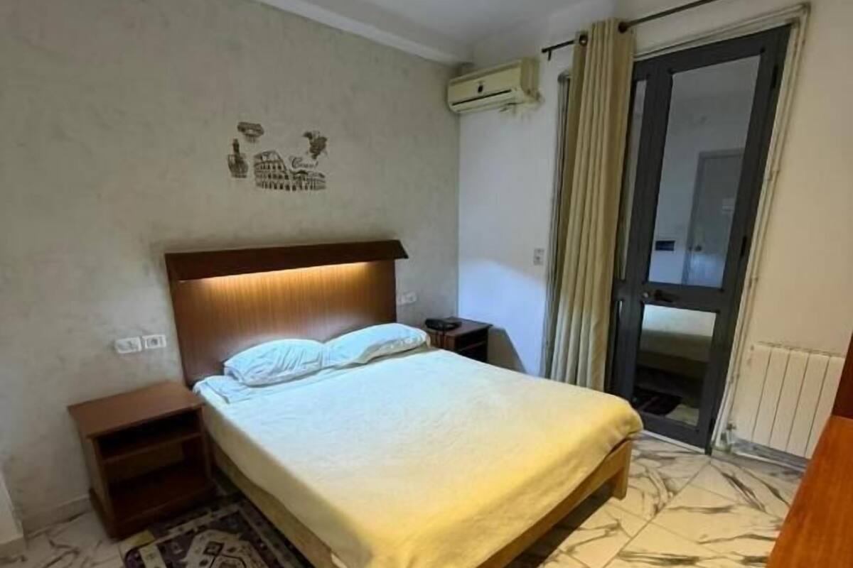 Une chambre à coucher avec un lit, une table de chevet et une fenêtre avec des rideaux.