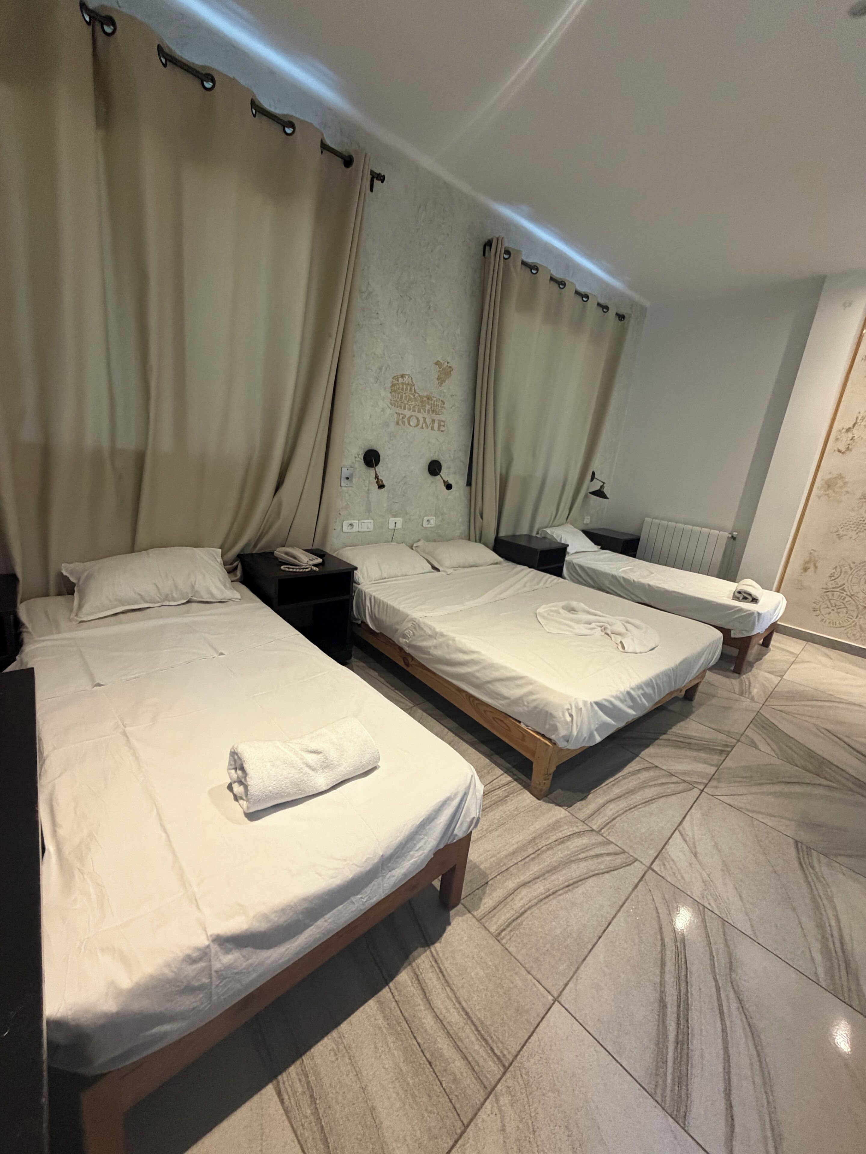 A hotel room with two single beds, a wooden headboard, a wall-mounted phone, and a radiator.