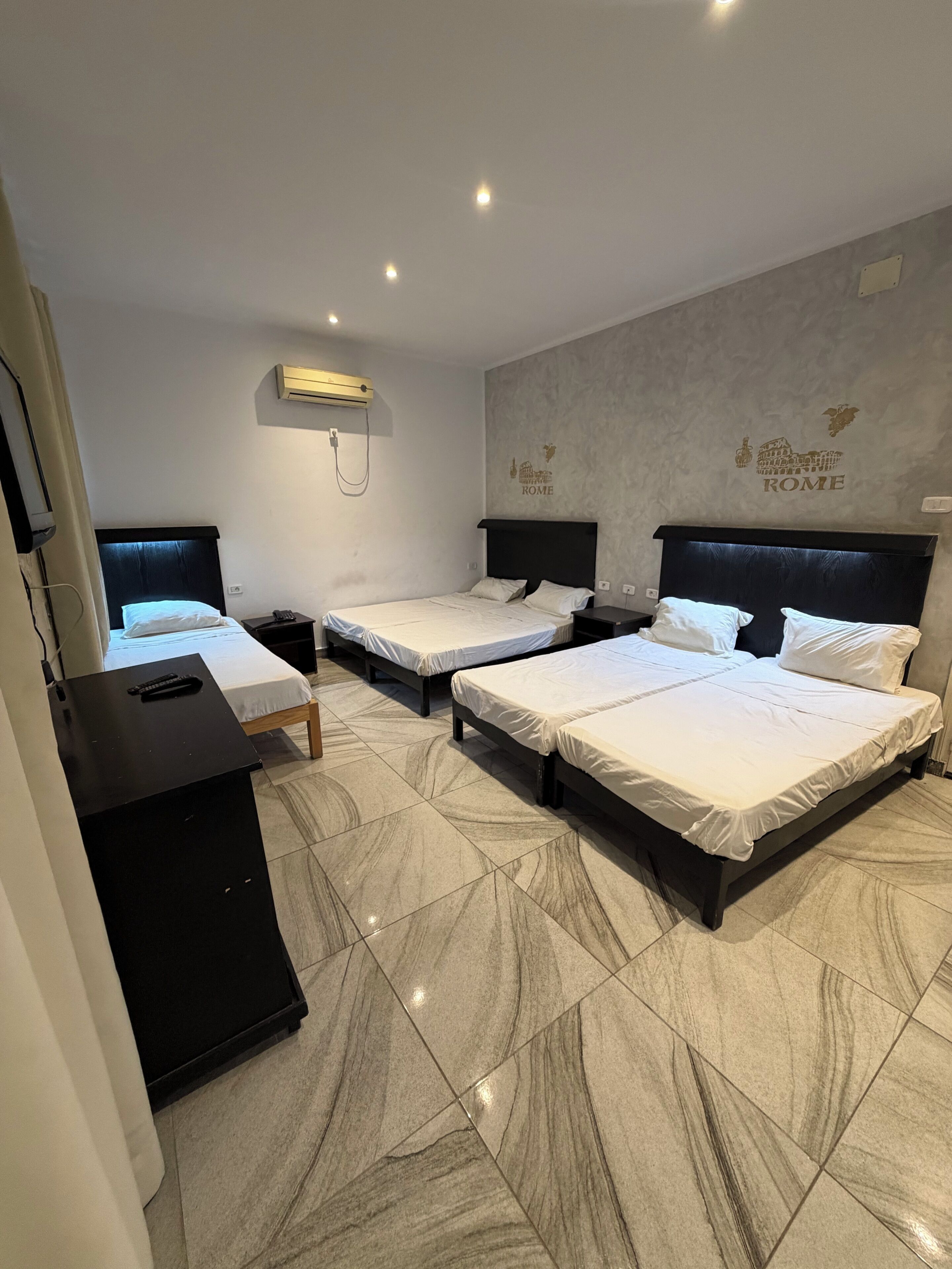 Ein Hotelzimmer mit drei Betten, einem Fernseher und einer Klimaanlage.