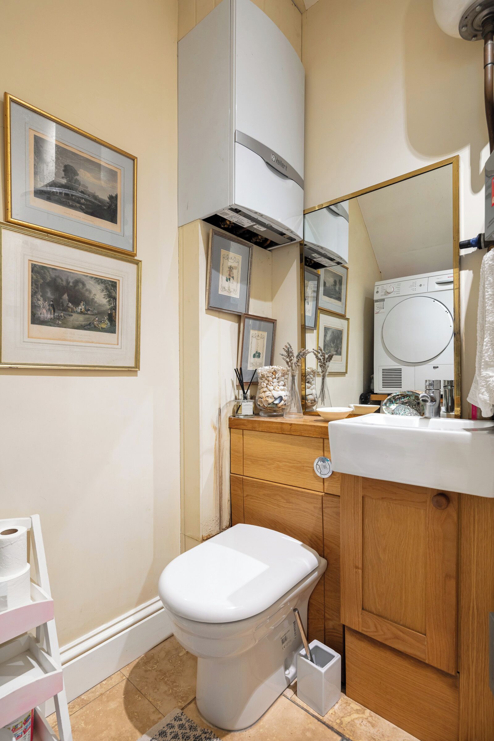 A bathroom with a toilet, vanity, mirror, framed pictures, and a washing machine.