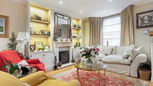 Una sala de estar con chimenea, un sofá, un sillón rojo, una mesa de centro de cristal y una alfombra estampada.
