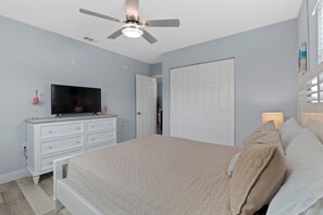 Een slaapkamer met een bed, een televisie, een dressoir, een plafondventilator en een deur.